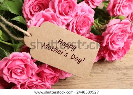 Happy Mother's Day greeting label and beautiful rose flowers on wooden table