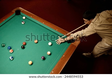 Minimal top view of Asian man playing billiards and hitting ball with cue stick copy space Royalty-Free Stock Photo #2448594553