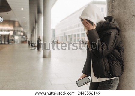Upset and depressed girl holding smartphone and holding head. University sad student suffering from depression at high school. Lonely bullied teen. Royalty-Free Stock Photo #2448596149