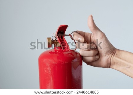 Red fire extinguisher with female hand, on gray background.