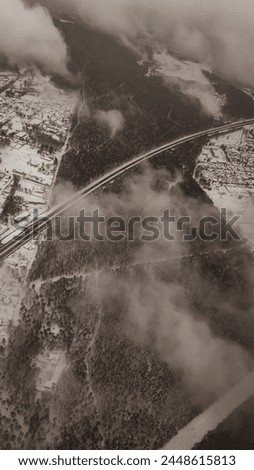 Aerial view of woods and snowy landscape from an aeroplane through light clouds. Pictures colours of black and white make it a unique piece of view of a landscape in the snowy winter.