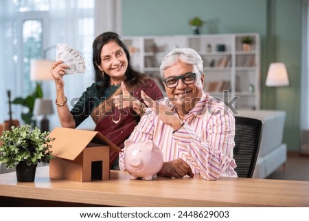 Retired Indian asian couple do paperwork at home with laptop, piggy bank, currency notes, documents Royalty-Free Stock Photo #2448629003