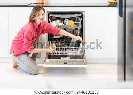 Busy housewife putting dirty plates in dishwasher machine in the kitchen. Household and exhausting cleaning day concept Royalty-Free Stock Photo #2448631239