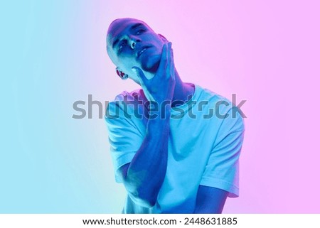 Handsome young man with bald head, shaved face and well-kept skin posing on gradient blue pink background in neon light. Concept of male beauty, body, youth, fitness, sport, health Royalty-Free Stock Photo #2448631885