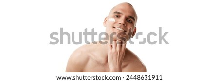 Handsome smiling young man with spotless, well-kept skin with moisturizing cream isolated on white studio background. Concept of skincare, male beauty, wellness, cosmetics, self-care. Banner Royalty-Free Stock Photo #2448631911
