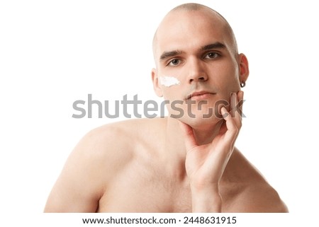 Handsome shitless young man with moisturizing cream on face isolated on white studio background. Spotless well-kept skin. Concept of skincare, male beauty, wellness, cosmetics, self-care Royalty-Free Stock Photo #2448631915