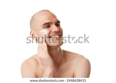 Handsome smiling young man with spotless, well-kept skin applying moisturizing cream isolated on white studio background. Concept of skincare, male beauty, wellness, cosmetics, self-care Royalty-Free Stock Photo #2448638415