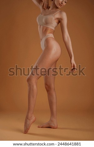 Showing the side, standing. Woman with slim body shape is posing against background.