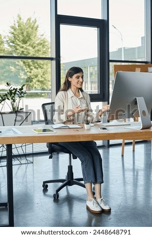 A businesswoman sits at a desk in a modern office, working on a computer.