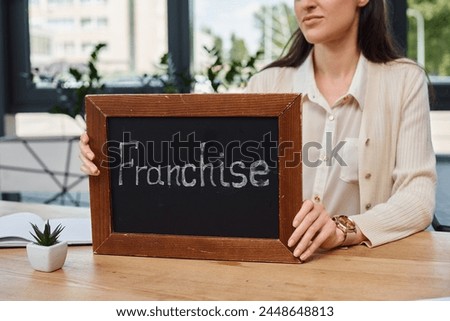 A businesswoman in a modern office sits at a table, holding a sign.
