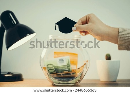 Transparent glass money box with euro banknotes inside, picture of students hat above, close up, toned. Concept of investing funds into education, savings for future knowledge