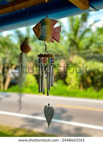 A hand-painted fish wind chime with metal tubes and beads hanging outdoors, a whimsical addition to garden decor Royalty-Free Stock Photo #2448663161