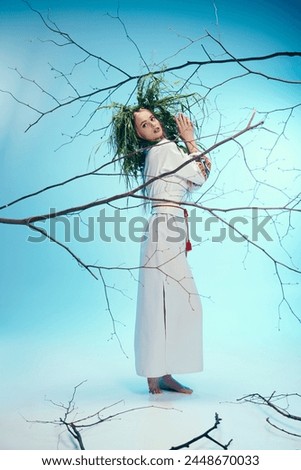 A young mavka in traditional attire stands gracefully in front of a twisted tree branch in a fairy and fantasy studio setting. Royalty-Free Stock Photo #2448670033