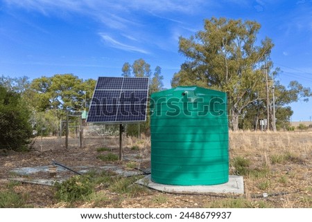 Large green plastic storage tank with solar panes connected to a borehole. Concept for extracting groundwater in locations where pumped water and electricity is not available.   Royalty-Free Stock Photo #2448679937