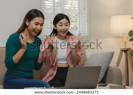 Two beautiful Asian teenage girls are having fun watching entertainment together at home on the sofa, Two beautiful female friends spend a weekend together in ultimate bliss in an apartment.