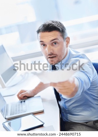 Business man, giving document at desk in office with tech for share information or present ideas on project. Serious editor, laptop and tablet in workspace and give paperwork in deadline review