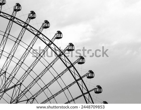 A black and white photo of a Ferris wheel with many small cabins. Scene is nostalgic and peaceful