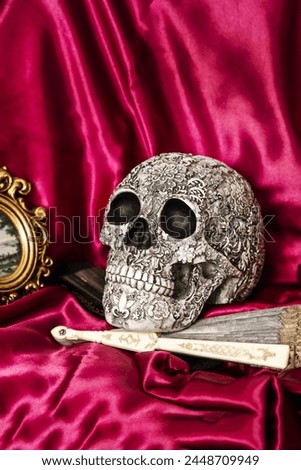 Still life with decorative skull on a fan and a red satin cloth along with other objects