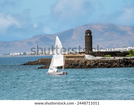 Sailing past the historical volcanic stone lighthouse at the entrance of the Arrecife harbor, Lanzarote, Canary Islands, Spain