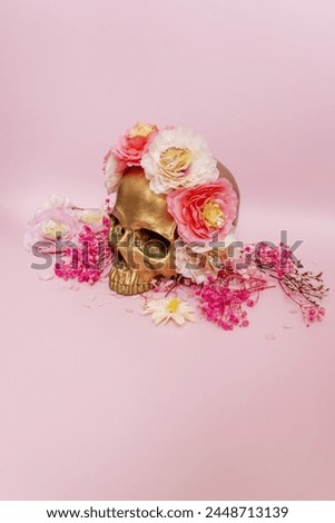 A golden skull adorned with flowers on a smooth pink surface