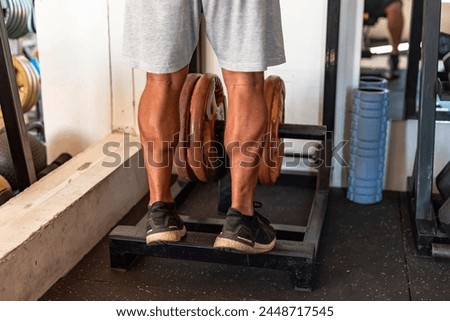 Dedicated anonymous man at the gym setting does calf raises on a weight-loaded machine with plates, focusing on lower body strength. Royalty-Free Stock Photo #2448717545