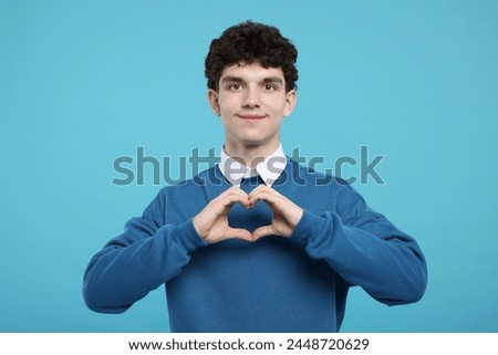 Happy young man showing heart gesture with hands on light blue background