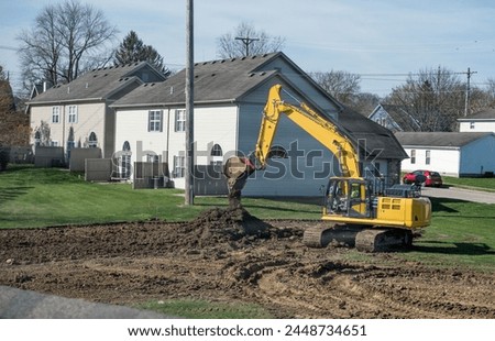 Excavator or backhoe dumping excavated soil into a pile at housing construction site in early morning light.