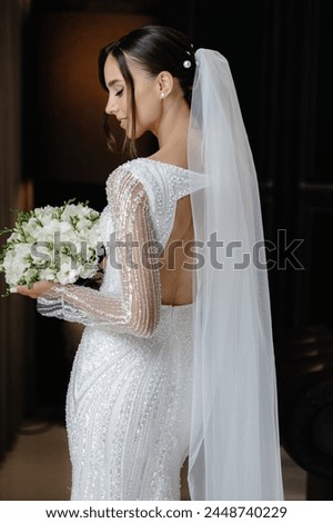 Stunning bride in elegant white dress and long veil, holding a bouquet of white roses against a dramatic black background. Ideal for wedding or bridal magazine cover.