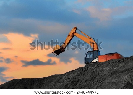 Coal mining in an open pit. Mining excavator loads coal in haul truck in quarry. Excavator digging in open pit coal mine. Excavator in open-pit on sunset background. Heavy machinery in opencast.  Royalty-Free Stock Photo #2448744971