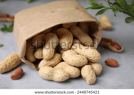 Paper bag with fresh unpeeled peanuts on grey table, closeup