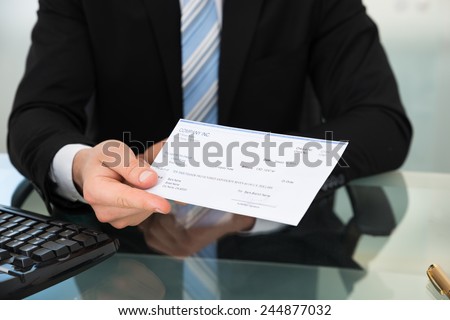 Midsection of businessman showing cheque at desk in office