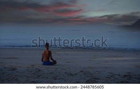 Man meditates or doing yoga exercise on the sandy beach in the evening. View from the back.