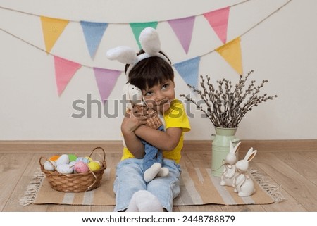 Easter photo shoot.A child wearing bunny ears holds an Easter bunny in his hands.Multi-colored Easter eggs lie in abasket and child sits next to him.