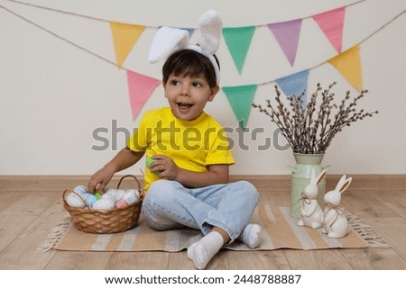 Easter photo shoot.A child holds Easter eggs in his hands.A boy with bunny ears on his head sits next to a basket of Easter eggs.