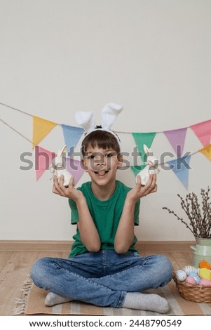 Easter photo shoot.A child holds an Easter bunny in his hands and smiles.A child sits on the floor next to Easter eggs in a basket.