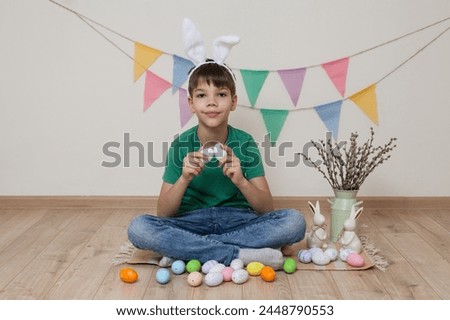 Easter photo shoot.A child holds Easter eggs in his hands.A boy with bunny ears on his head sits next to a basket of Easter eggs.