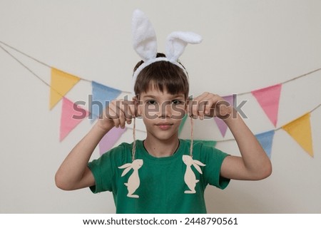 Easter photo shoot.A child holds an Easter bunny in his hands and smiles.A child wearing bunny ears on his head holds figurines of rabbits in his hands close-up