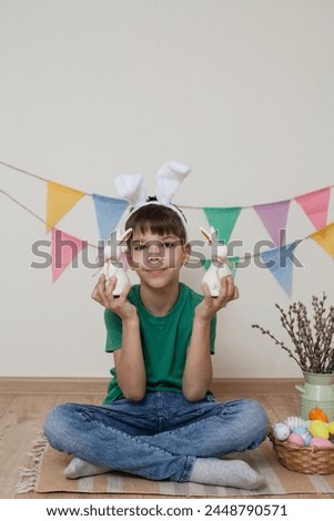 Easter photo shoot.A child holds an Easter bunny in his hands and smiles.A child sits on the floor next to Easter eggs in a basket.