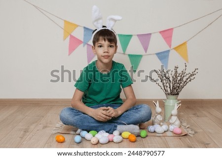A child wearing bunny ears on his head sits next to a basket and Easter eggs.Easter photo shoot.