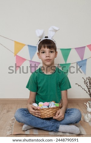 Easter photo shoot.A child holds a basket of Easter eggs in his hands.A boy wearing bunny ears sits on the floor.