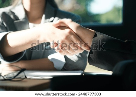 Two people shaking hands in a business meeting. The woman on the left is wearing glasses. The man on the right is wearing a suit