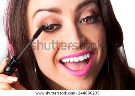 Young Pretty Latino Woman Putting on mascara while listening to Headphones