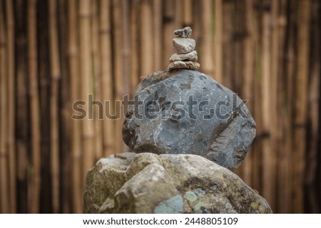 A stack of balanced rocks sits in the forefront of a bamboo wall inside of a wooden room. Royalty-Free Stock Photo #2448805109