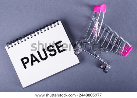 A shopping cart rests next to a notebook with the word pause written on it, reflecting a moment of rest or break in daily activities.