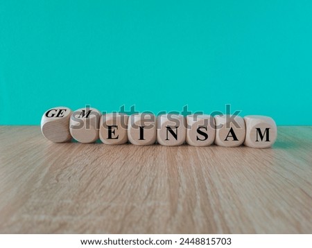 Turned a wooden cube and changes the German word 'einsam' (lonely) to 'gemeinsam' (together). Beautiful blue background, wooden table. Copy space.