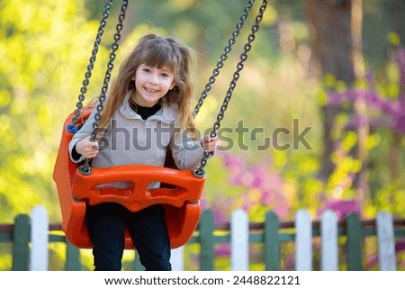 Cute blonde girl having fun swinging on a swing in the playground