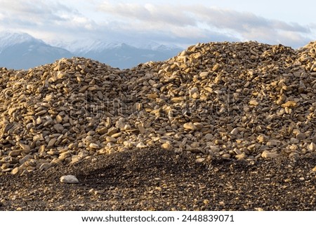 A pile of slag on the ground against the background of mountain peaks and a blue cloudy sky. A heap of building materials. Construction site. Carpathian Mountains in Romania