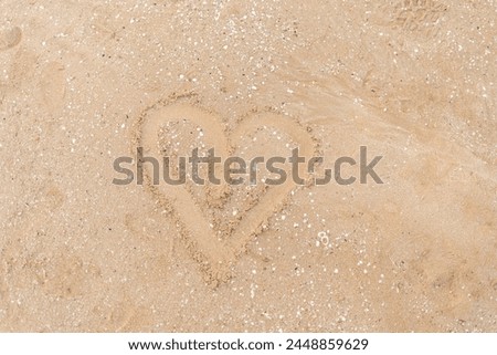 An intricately drawn heart shape stands out on the sandy beach, encapsulating the timeless allure of romantic gestures amidst nature's simplicity.
