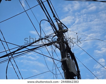 Tangle of electrical wires and utility pole set against a cloud-speckled blue sky.