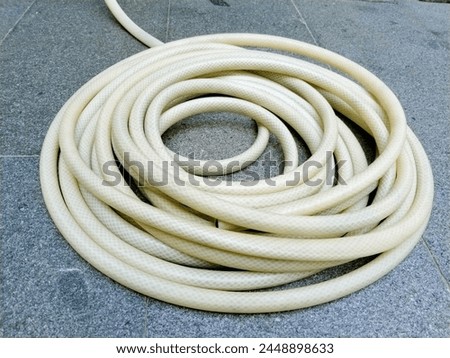 The white water hose is tightly coiled, on a soft gray natural stone floor with a rough texture